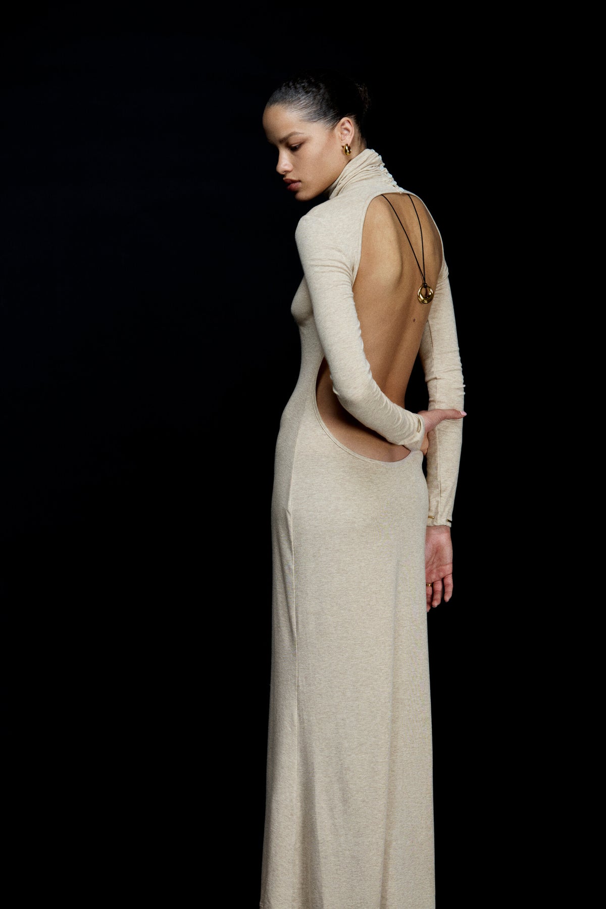Woman wearing a long, light-colored dress with cut-out design on a black background