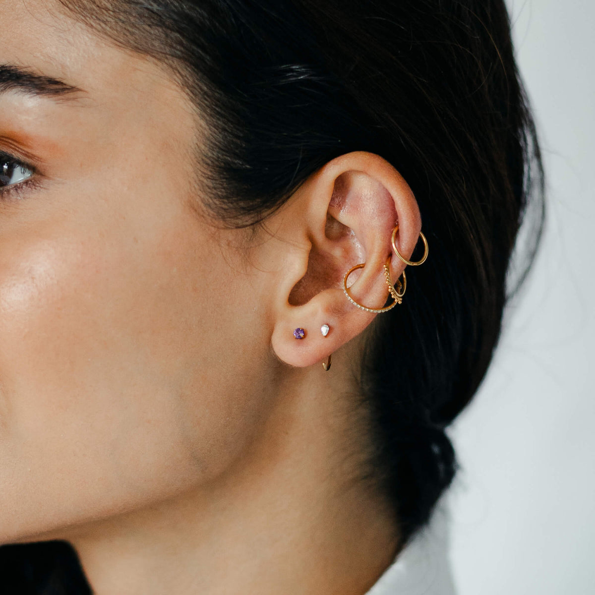 Classic, Siren and Eternity Cartilage Hoop, Pear Open Huggie Hoop and Amethyst Nap Earrings on model (Gold)