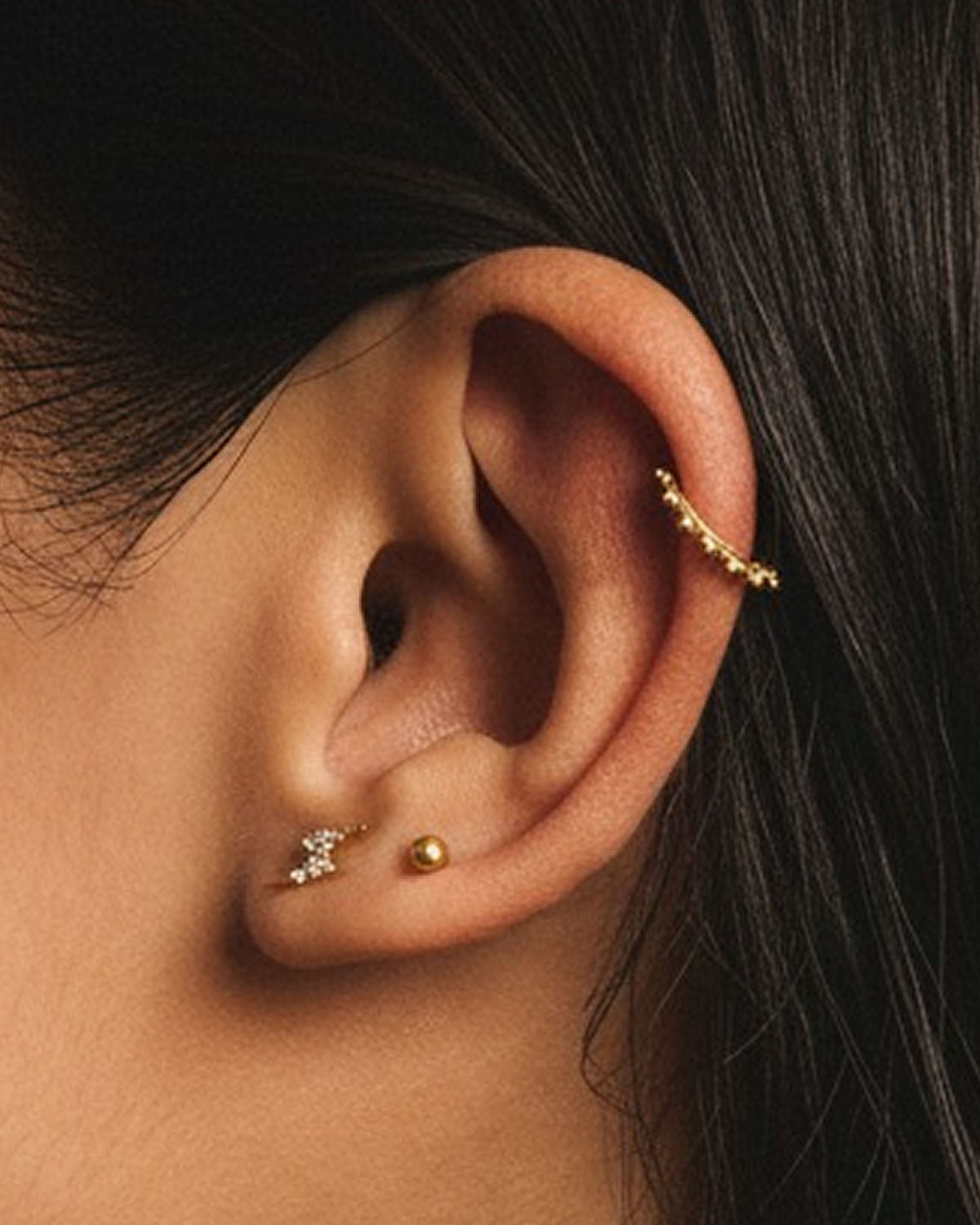 Close-up of an ear styled with a gold beaded ear climber and crystal studs