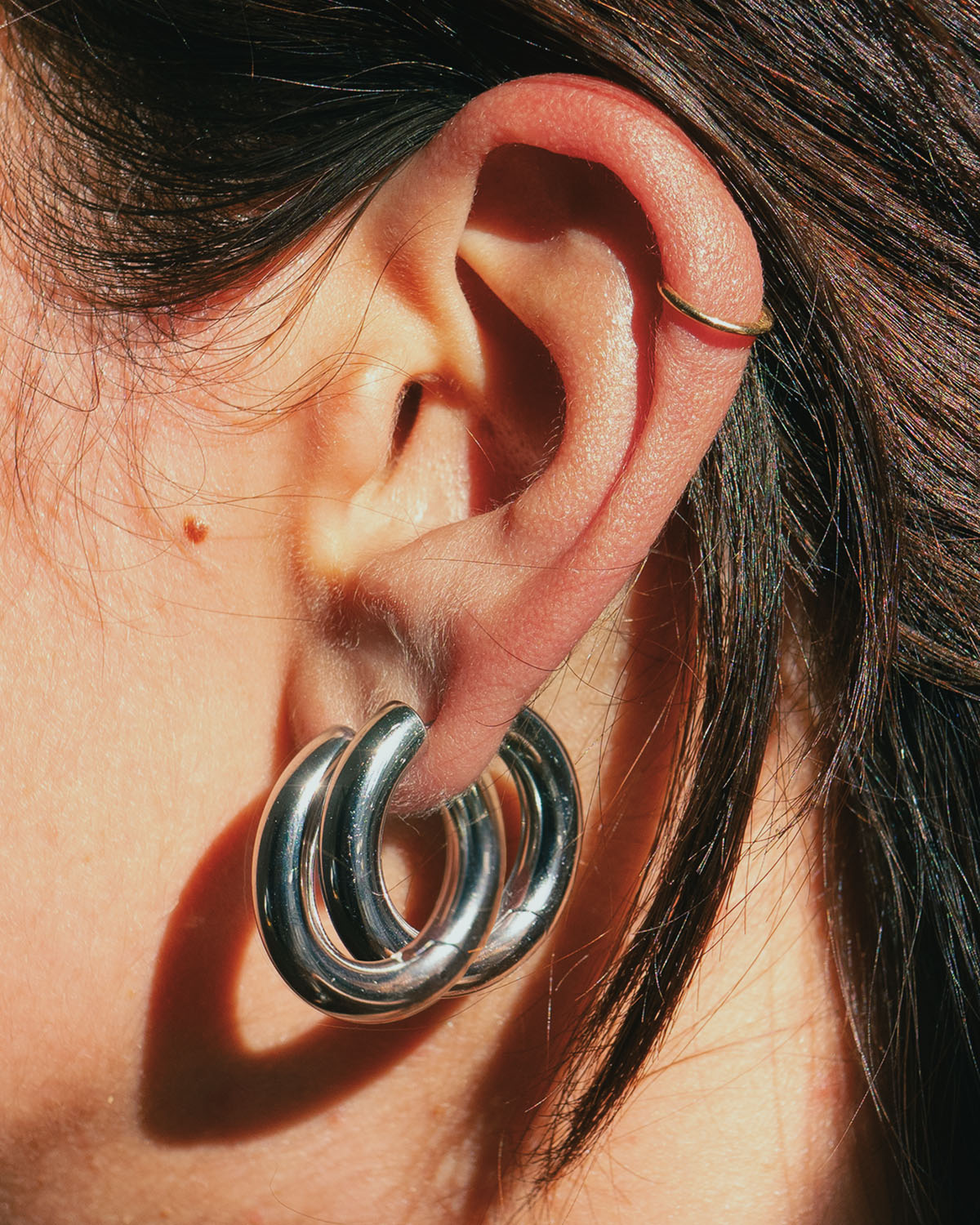 Close-up of an ear with chunky silver hoops and a thin gold ear cuff