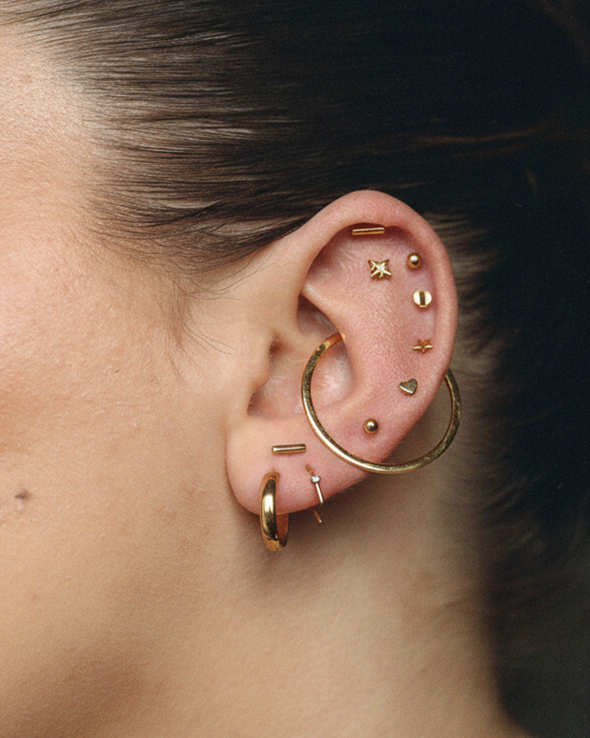 Close-up of a curated ear stack with gold hoops and tiny star and heart studs
