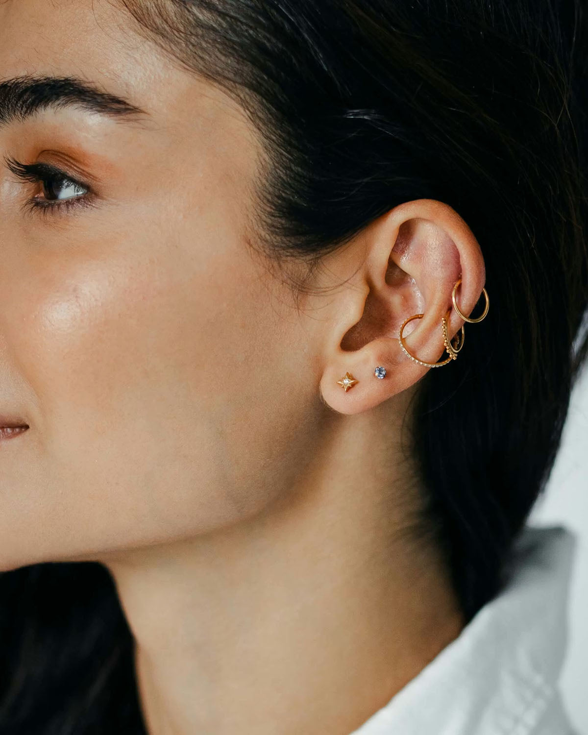 Close-up of an ear styled with gold huggie hoops, ear cuffs, and a star stud