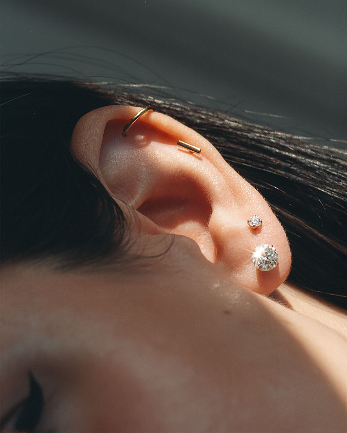 Close-up of an ear with a gold cartilage hoop and crystal studs
